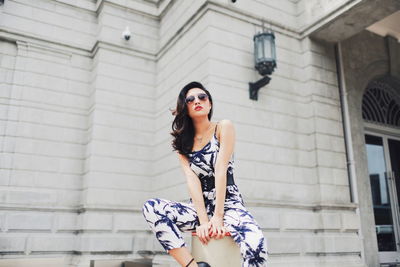 Woman sitting on bollard against building