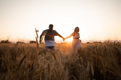 Friends standing on field against sky during sunset