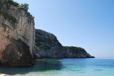 Rock formations by sea against clear blue sky