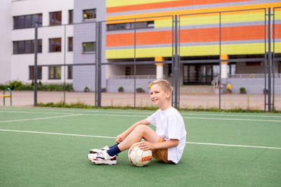 A boy holds a soccer ball while sitting on a soccer field