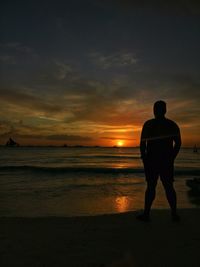 Silhouette man standing on beach against sky during sunset