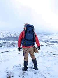 Rear view of man walking on snowcapped mountain against sky