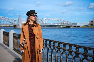 Woman standing by railing against bridge against sky