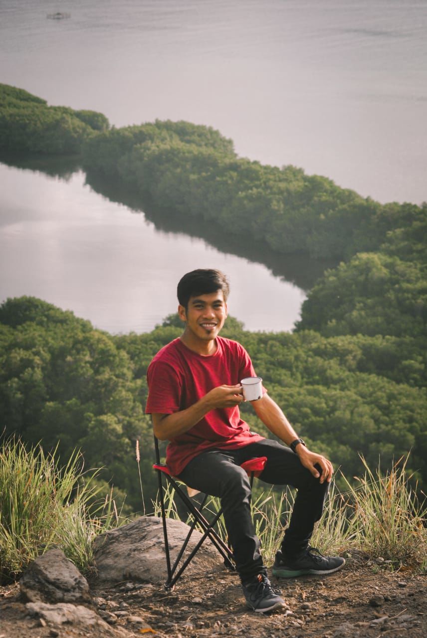 sitting, one person, full length, nature, adult, plant, leisure activity, relaxation, young adult, tree, men, land, water, lifestyles, casual clothing, landscape, environment, forest, smiling, holiday, outdoors, music, vacation, tranquility, trip, mountain, happiness, activity, day, beauty in nature, sky, travel, musical instrument, person, clothing, looking, adventure, lake, rural scene, front view, recreation, scenics - nature