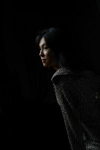 Woman looking away while standing against black background