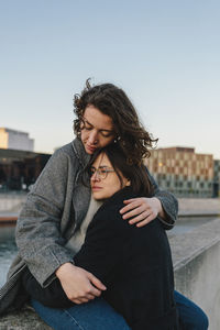 Lesbian couple embracing at rooftop against clear sky