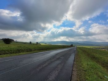 Empty road amidst field against sky