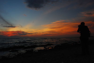 Silhouette people looking at sea against sky during sunset