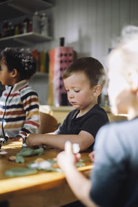 Schoolboy playing with clay while sitting at bench during art class at kindergarten