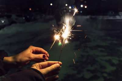 Cropped hand holding sparkler at night