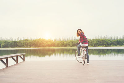 Woman riding bicycle on pier over lake against sky