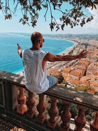 Rear view of man sitting on railing against town