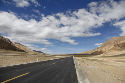 A flat, newly built wide asphalt road leads to the beautiful mountains in the distance