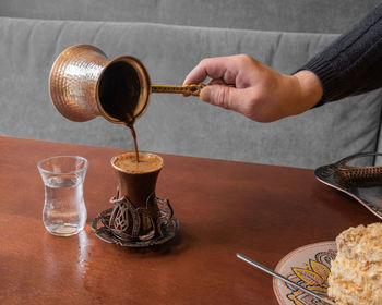 Midsection of person pouring wine in glass on table