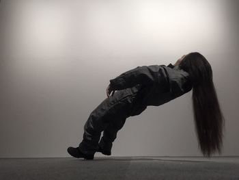Side view of woman with long hair balancing in mid-air against wall