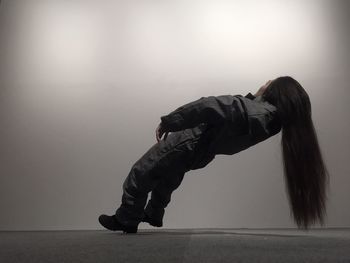 Side view of woman with long hair balancing in mid-air against wall