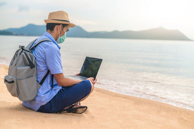 Young woman using laptop while sitting at beach