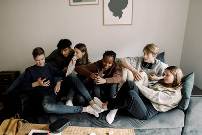 Multi-ethnic teenage friends using smart phones while spending leisure time at home