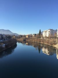 Reflection of buildings in lake against clear blue sky