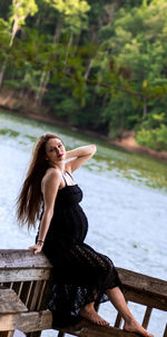 Beautiful young woman looking away while standing on railing against lake