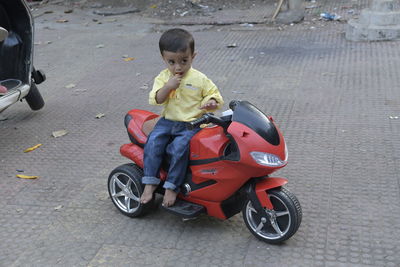 Full length of a small boy riding toy car on road with fruit juice in his hand