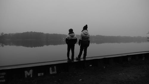 Full length of mother and son stand on the wall and look at the lake against sky