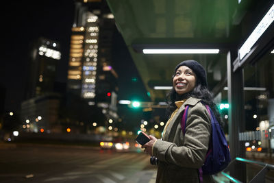 Portrait of smiling woman standing in city at night