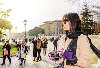 Woman holding camera while traveling in city