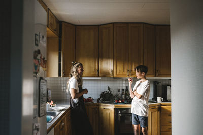 Son eating apple standing with mother in kitchen at home