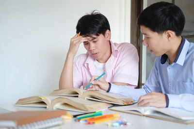 Young man assisting friend in studying at table in classroom
