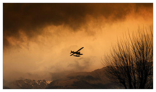 Silhouette plane flying against cloudy sky