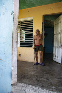 Portrait of shirtless man standing against door