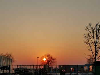 Silhouette bare trees by street against sky during sunset