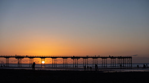 Silhouette cranes on beach against clear sky during sunset