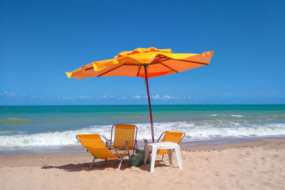 Deck chairs on beach against clear blue sky