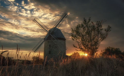 Traditional windmill on field against sky during sunset