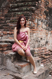 Portrait of smiling woman sitting against brick wall