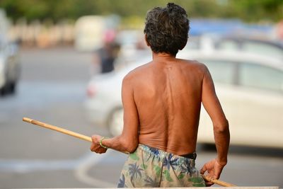 Rear view of shirtless man holding stick