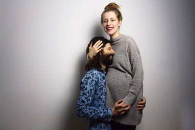 Smiling man embracing pregnant woman standing against gray background