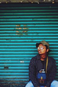 Young man sitting against closed shutter