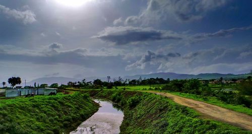 Scenic view of canal amidst grassy field against cloudy sky