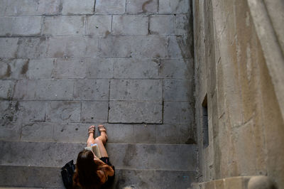 Directly above shot of young woman reading book while sitting on steps by wall