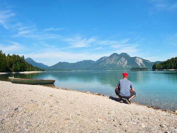 Adult man in blue shirt at old fishing paddle boat at mountains lake coast. sunny spring day.