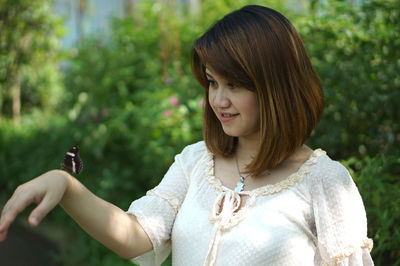 Young woman with butterfly on hand against plants