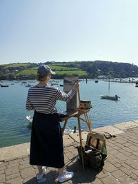 Rear view of man standing by sea against clear sky