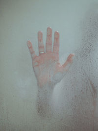 Close-up of hand on wet glass against white background