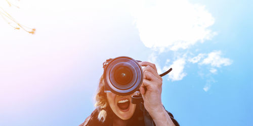 Midsection of person holding camera against sky