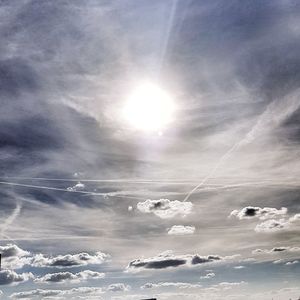 Low angle view of sun shining on cloudy sky