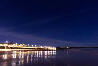 Illuminated buildings by sea against sky at night