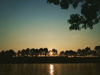 Silhouette trees by lake against clear sky during sunset